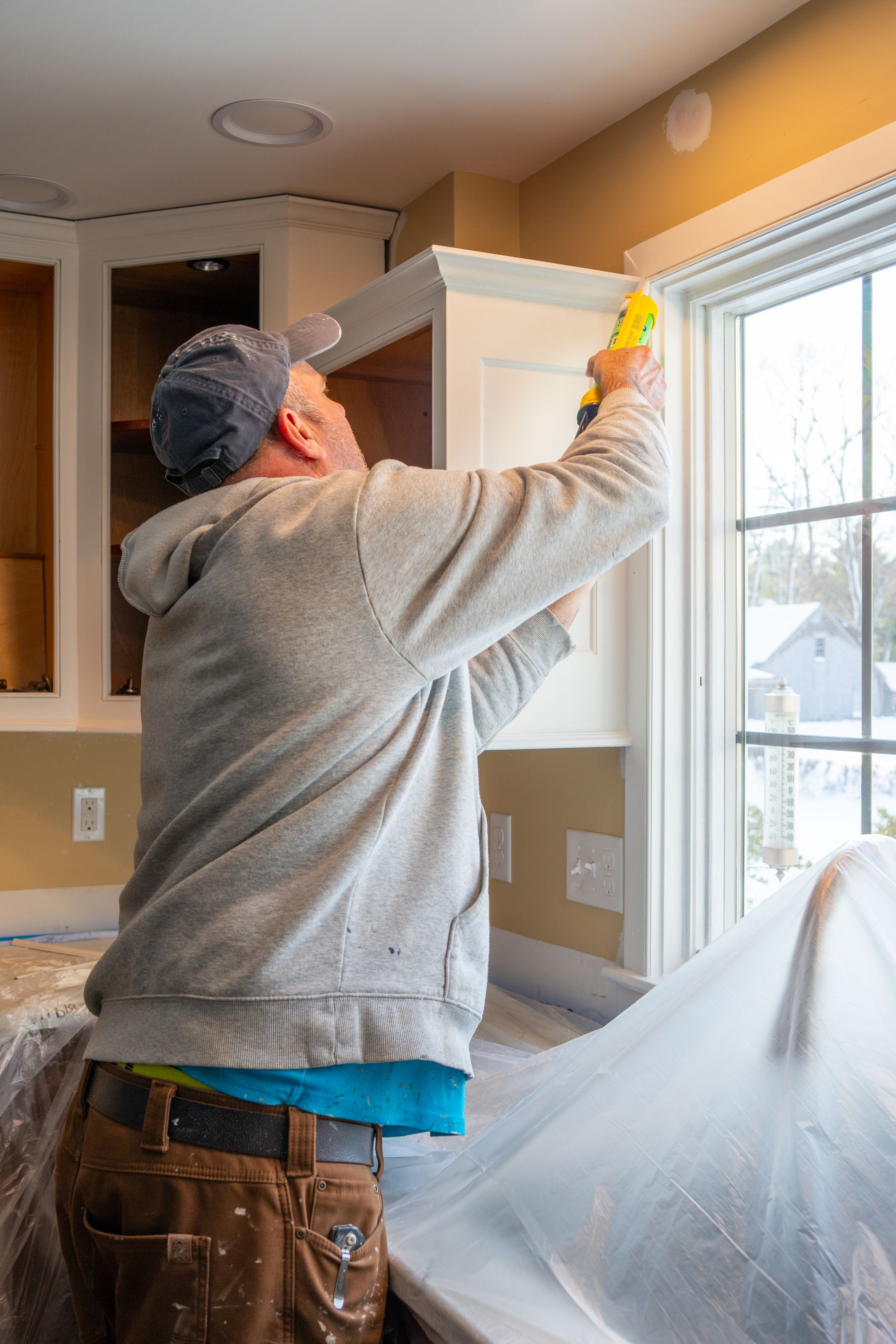 Worker caulking trim beside a kitchen cabinet