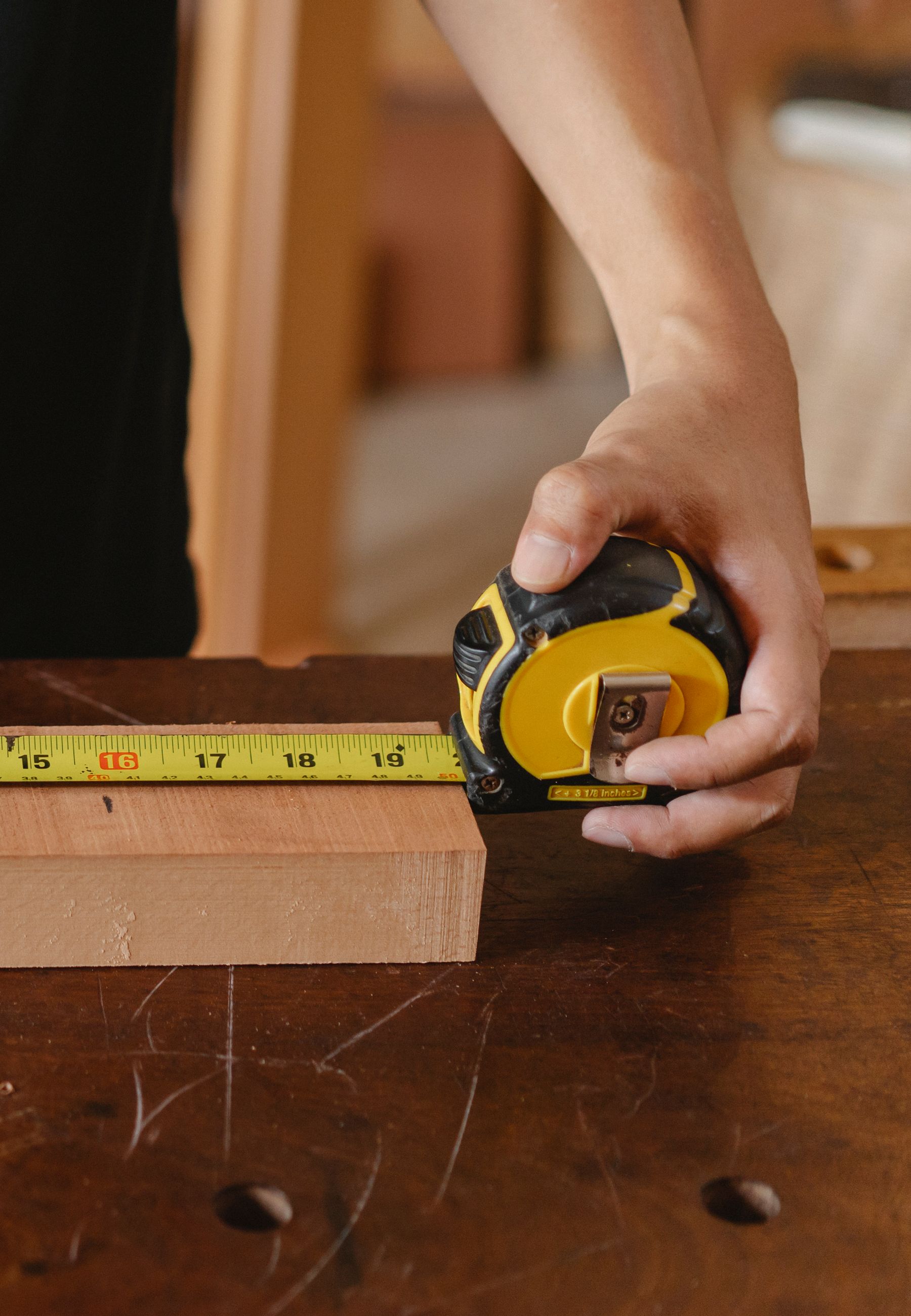 Hands measuring a wood board with a tape measure